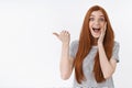 Amused happy cheerful surprised young cute redhead girl blue eyes drop jaw pointing left thumb excited standing Royalty Free Stock Photo