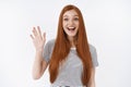 Amused outgoing lively redhead cute girl blue eyes widen eyes happily waving raised palm hello hi welcome gesture