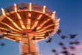 Amusement park motion blurred riders on brightly lit retro vintage tilting swing at blue hour. Royalty Free Stock Photo