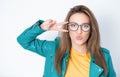 Amusing girl shows peace sing with fingers and send kiss to you, wearing green leather jacket, isolated on white background.