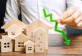 Analyst holds down arrow near the wooden houses. Concept of falling real estate market. Low prices and cost of housing. Reduced Royalty Free Stock Photo