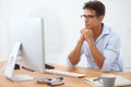 Analyzing the numbers...A handsome young businessman wearing glasses looking thoughtfully at his computer screen. Royalty Free Stock Photo