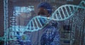 Analyzing scientist wearing blue cap mask scrubs in high-tech lab, with DNA helix and code overlays Royalty Free Stock Photo