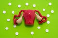 Anatomical model of female uterus with ovaries is on green background with white tablets around, forming ornament in polka dots. C