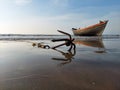 An anchor knoted with rope lying on Mandarmani beach with a background of a fishingh boat.