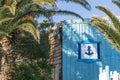 Anchor symbol of summer sea tourism and holidays on the beautiful wooden blue fence with entrance door in the shadow of palm tree Royalty Free Stock Photo