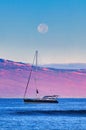 Anchored silhouetted boat in Lahaina harbor on Maui with setting full moon.