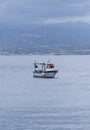 an anchored small white boat in middle of milazzo bay with sicilian mountains