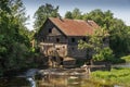 Ancient abandoned water mill surrounded by beautiful nature. House built of stone and wood, exterior walls and dilapidated bridge Royalty Free Stock Photo