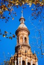 Ancient architecture tower view in Plaza de EspaÃÂ±a against blue sunny clear sky framed by tree leaves. Main landmark popular