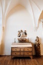 Ancient chest of drawers with candlesticks and dried flowers with several statues nearby.