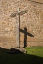 Ancient cross on stone wall. Stone old crucifix with shadow on monastery backyard. Christianity symbols. Medieval cemetery. Royalty Free Stock Photo