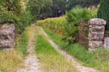 Ancient damaged gate with trail to the forest. Old stone fence and iron gate near corn field. Walk in abandoned places, France. Royalty Free Stock Photo