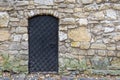 An ancient door in black with a large lattice texture with large rivets against the background of a wall and a non-hewn granite st Royalty Free Stock Photo