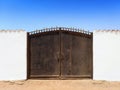 Ancient Egyptian wrought iron gate with old white cement wall under blue sky. Oasis and Berber constructions in the desert