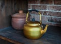 Ancient gold kettle on old wooden shelf. Classic teapots to use for drinking tea or coffee. Clay pot in the background