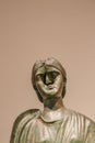 Ancient Greek brass sculpture of woman with a bashed in face against tan background - room for copy Royalty Free Stock Photo