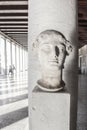 Ancient Greek Bust on pedestal near Acropolis in Athens Greece with unrecognizable tourists walking through shadows of the pillars