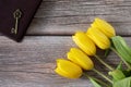 Ancient key on closed holy bible book and yellow tulips on wooden table, top view