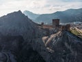 Ancient medieval Genoese fortress tower on mountain range rocks above sea, aerial view from drone