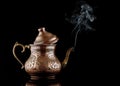 Ancient oriental copper teapot with white smoke isolated on a black background