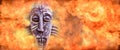 ancient primitive wooden mask surrounded by a solid wall of flame