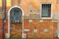 Ancient red brick wall with two windows. Canal with turquoise water flows under the wall. Venice, Italy Royalty Free Stock Photo