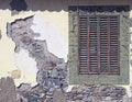 an ancient red wooden shuttered window in a frame with peeling faded green paint in an old house wall with broken cracked cement Royalty Free Stock Photo