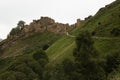 Ancient ruin of stone impregnable, destruction city on peak of mountain in highlands in Dagestan with green slope, old dirt road.