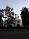 White Orthodox Church, hidden behind dark fir trees in the rays of the setting sun.