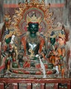 An ancient statue of a green Tibetan deity in the lotus position surrounded by four deities