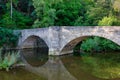 An ancient stone bridge mirroring in a small creek with trees in the backgrou Royalty Free Stock Photo