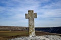 Ancient stone Christian cross, mounted on cliff, near rock monastery, against blue sky. Old Orhei, Moldova