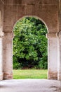 Ancient stone masonry arch, under the portico beyond which you can see an imposing magnolia grandiflora tree in a green lawn. Royalty Free Stock Photo