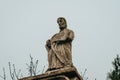 Ancient stone statue of man with a staff and plate with the inscription. Gray sky background