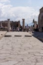 Ancient stone street with columns and statue and tourists in Pompeii, Italy. Antique culture concept. Pompeii ruins. Royalty Free Stock Photo