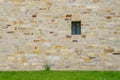 An ancient stone wall of hewn stone with a small window. Green grass Royalty Free Stock Photo