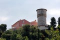 Ancient style defense tower on top of hill made of stone blocks next to large new houses surrounded with forest Royalty Free Stock Photo