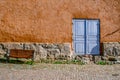 An ancient textured wall with a stone basement, a blue door and a bench.