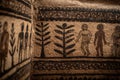 Ancient wall carvings depict human figures and trees with intricate patterns in a textured stone setting Royalty Free Stock Photo