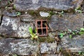 Ancient wall made of natural rocks with window-like water-drain pipe in the center and with plants and lichens between blocks Royalty Free Stock Photo