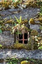 Ancient wall made of natural rocks with window-like water-drain pipe in the center and with plants and lichens between blocks Royalty Free Stock Photo