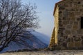 An ancient, ancient wall of stones against the background of mountains. Nearby is a tree without leaves.