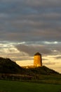 Ancient windmill stands in a grassy field at dusk under cloudy skies Royalty Free Stock Photo