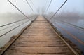 Ancient wooden suspension bridge in the dense fog.