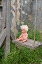 Ancient wooden swing on ropes. A plastic naked doll on a swing.