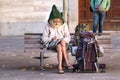 A senior man backpacker sitting on a square bench, is writing down notes on a notepad wearing eyeglasses and a gnome wool hat