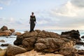 Androgynous black divine person poses on scenic ocean beach. Non-binary ethnic fashion model in long posh dress and