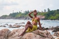 Androgynous black fashion model poses on scenic ocean beach at sunset. Non-binary ethnic fashion model in long revealing