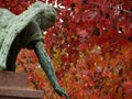 Angel in a bronze sculpture at the Montparnasse cemetery in Paris. In the background a tree with red leaves